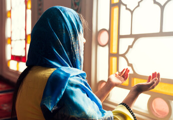 Muslim woman in headscarf praying with her hands open in the mosque