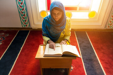 Young muslim woman reading Quran in the mosque. woman praying and reading quran in mosque during...