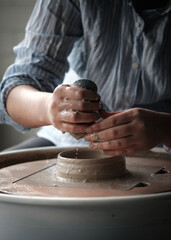 Unrecognizable Ceramics Maker working with Pottery Wheel in Cozy Workshop Adding Water to Future...