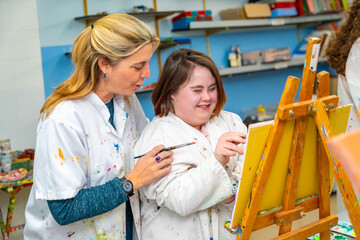 Teacher helping a woman with down syndrome during painting class