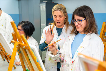 Disabled woman painting in a canvas next to a teacher