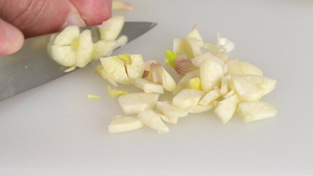 The chef chopping garlic on a white plastic cutting board, close-up view, preparation process