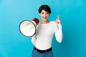 Woman with short hair isolated on blue background holding a megaphone and pointing up a great idea