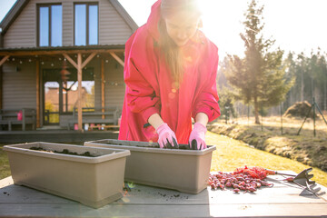 Woman in vibrant pink attire planting onion sets in a container garden during the crisp early...