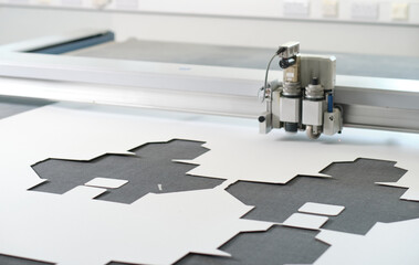 A laser cutting machine cutting out intricate design templates in a white clinical manufacture factory warehouse. Laser cutters in the industrial sector for accurate cutting results.