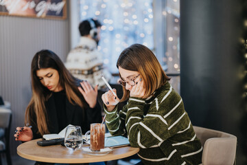 Two young women engaged in work, collaborating on notes and analysis in a relaxed, warmly lit cafe...