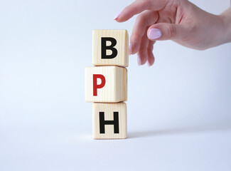 BPH - Benign Prostatic Hyperplasia symbol. Wooden cubes with word BPH. Businessman hand. Beautiful white background. Medical and BPH concept. Copy space.