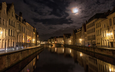 Fototapeta na wymiar Night shot of old canals and buildings in the medieval Flemish city of Bruges. View of the canals and the night city of Bruges, which is beautifully illuminated by the full moon.