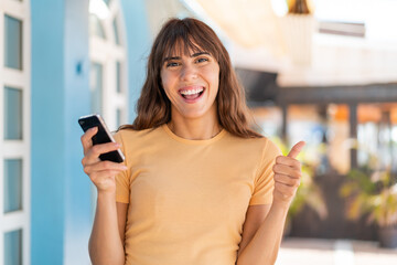 Young woman at outdoors using mobile phone while doing thumbs up