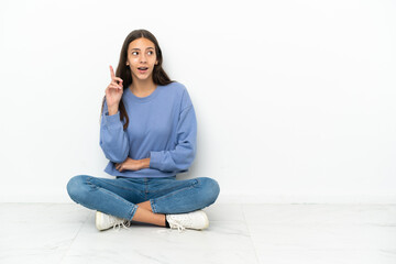 Young French girl sitting on the floor thinking an idea pointing the finger up