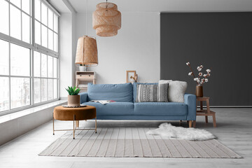Cozy interior of living room with blue sofa, pouf and and wicker ceiling lamp