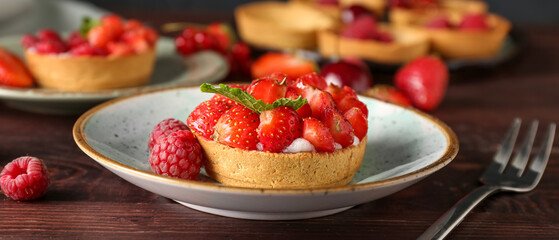 Plate with tasty berry tartlet on wooden table