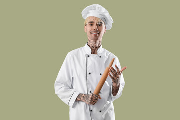 Tattooed male chef with rolling pin on green background
