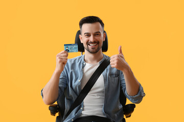 Handsome man with driver license showing thumb-up in car seat on yellow background - obrazy, fototapety, plakaty