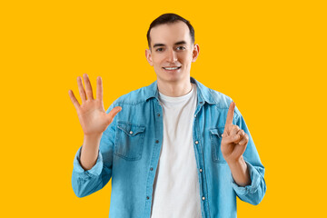 Young man showing six fingers on yellow background