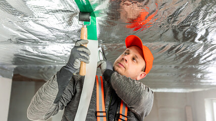 The builder is gluing the special tape on the joint of vapor barriers.  The vapor barrier as protection of thermal insulation against internal moisture.