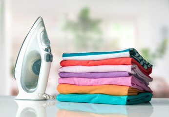 Colorful cotton shirts folded stack on table with iron. Household concept. Spring summer clothes.