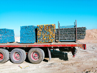 A truck is carrying a load of construction materials. The truck is red and white. The materials are stacked in various sizes and colors. scaffold