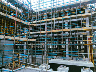 A construction site with scaffolding and workers. Scene is busy and active. The workers are focused on their tasks, and the scaffolding is being used to reach higher areas