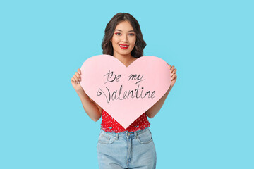 Beautiful young happy Asian woman with paper heart on blue background. Valentine's Day celebration