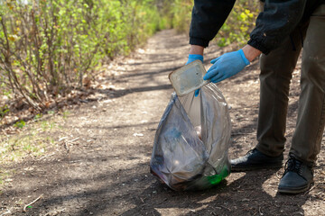 Man in gloves collects plastic trash in forest