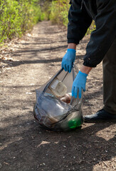 Man in gloves collects plastic trash in forest