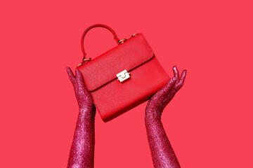 Female hands covered with glitter and stylish handbag on red background, closeup