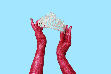 Female hands covered with glitter and beautiful tiara on color background, closeup