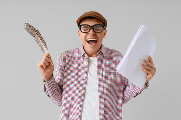 Happy male author with feather and paper sheets on light background