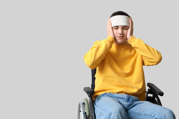 Young man with brain concussion in wheelchair on light background