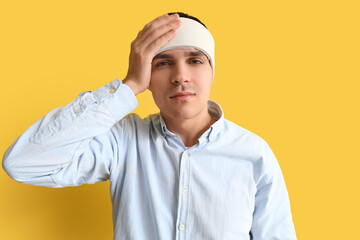 Young man with brain concussion and bandaged head on yellow background