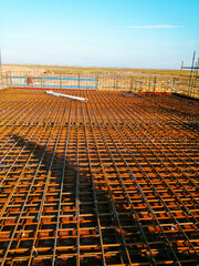 A construction site with a large area of metal mesh. The mesh is brown and the sky is blue