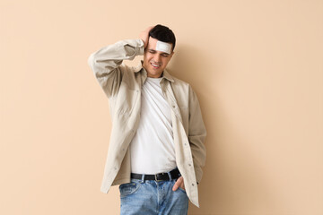 Young man with brain concussion and medical patch on beige background