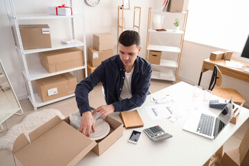 Male online store seller with box of dishes at table in warehouse