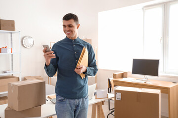 Male online store seller with mobile phone and envelopes in warehouse