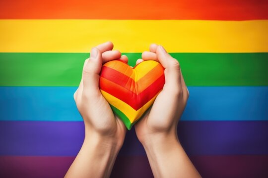 Hands holding heart shaped LGBT flag on rainbow background. LGBT concept. LGBT Concept with Copy Space. Pride Month Concept.