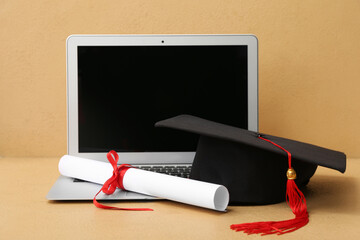 Mortar board with diploma and modern laptop on brown background