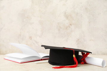 Mortar board with diploma and notebook on beige background
