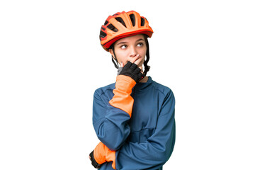 Teenager cyclist girl over isolated chroma key background having doubts and with confuse face expression