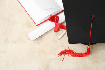 Mortar board with diploma and notebook on beige background