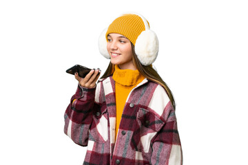 Teenager caucasian girl wearing winter muffs over isolated background keeping a conversation with...