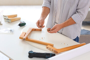 Young man with bolts assembling coffee table at home, closeup