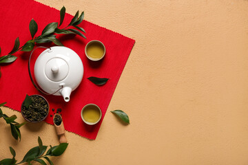 Teapot with cups, scoop of dry tea and leaves on beige grunge background