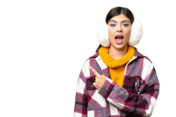 Young Russian woman wearing winter muffs over isolated chroma key background surprised and pointing...