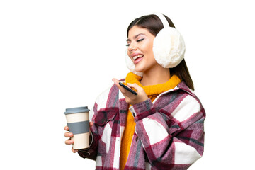 Young Russian woman wearing winter muffs over isolated chroma key background holding coffee to take...