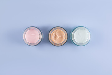 Three beautiful glass cosmetic jars with delicate texture of face and body care cream on a blue background. Top view. A copy space. presentation.