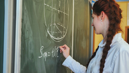 A red-haired schoolgirl draws geometric shapes on the board.