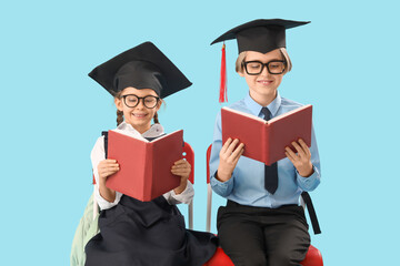 Little children in graduation hats reading books on blue background. End of school year