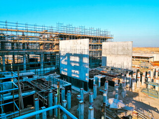 A construction site with scaffolding and a large building in the background. The sky is clear and blue