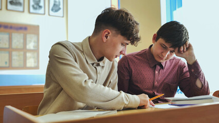 Schoolboys at a desk during class. - obrazy, fototapety, plakaty